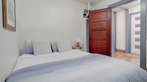 Una camera da letto con un letto, un comodino, una porta in legno e un'apertura che dà su un'altra stanza.