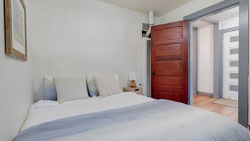 A bedroom with a bed, a nightstand, a wooden door, and an open door leading to another room.