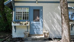 Una casa con una porta blu, una finestra con un balcone fiorito e un albero di fronte.