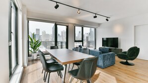 Uma sala de estar moderna com área de jantar, janelas amplas, televisão de tela plana e vista para a cidade.