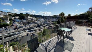 A rooftop terrace with a table and chairs, overlooking a cityscape with buildings and a church. - Ockendon House Apartment A (Torquay)