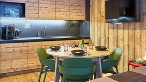 Eine moderne Küche mit Holzvertäfelung, einem Einbauofen, einer Kaffeemaschine und einem Essbereich mit grünen Stühlen.