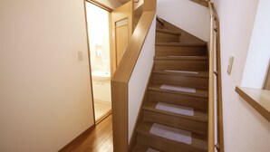 A wooden staircase with a handrail, leading to a room with a white door and a visible bathroom. - Honmachi 5-chome (Tokyo)