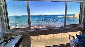Ein Zimmer mit großem Fenster mit Blick auf einen Strand und das Meer.