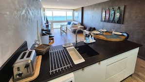 Eine moderne Küche mit einer großen Kochinsel, ein Essbereich mit Blick und ein Wohnbereich mit Sofa und Couchtisch.
