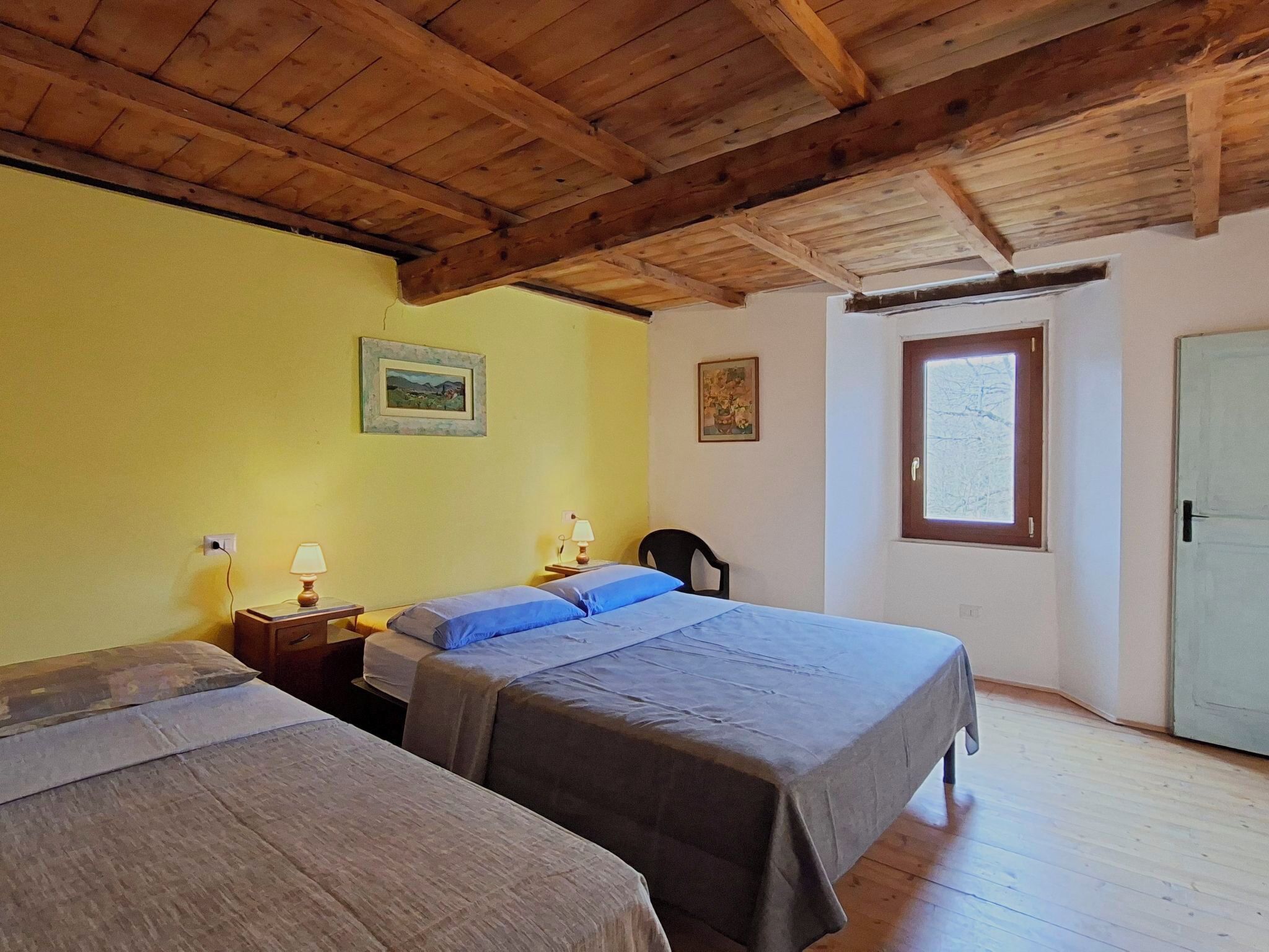Una habitación con dos camas, vigas de madera en el techo, una ventana y dos lámparas fijadas a la pared.