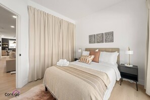 Un dormitorio moderno con una cama grande, una mesita de noche y vistas al área de estar contigua.