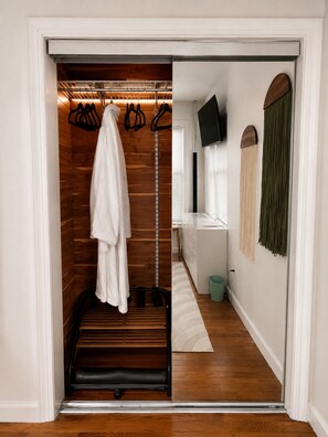 A walk-in closet with a hanging rack, a white robe, and a television on the wall. - Boutique 2BR ,20 Min NYC, Sleeps 6, Coffee Bar, Nintendo + Family Extras (West New York)