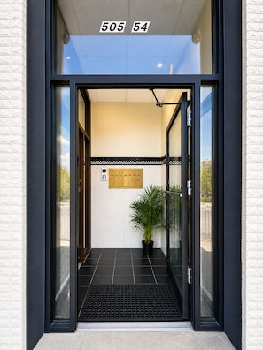 Una entrada moderna con puerta de vidrio, una planta en maceta y piso de baldosas.