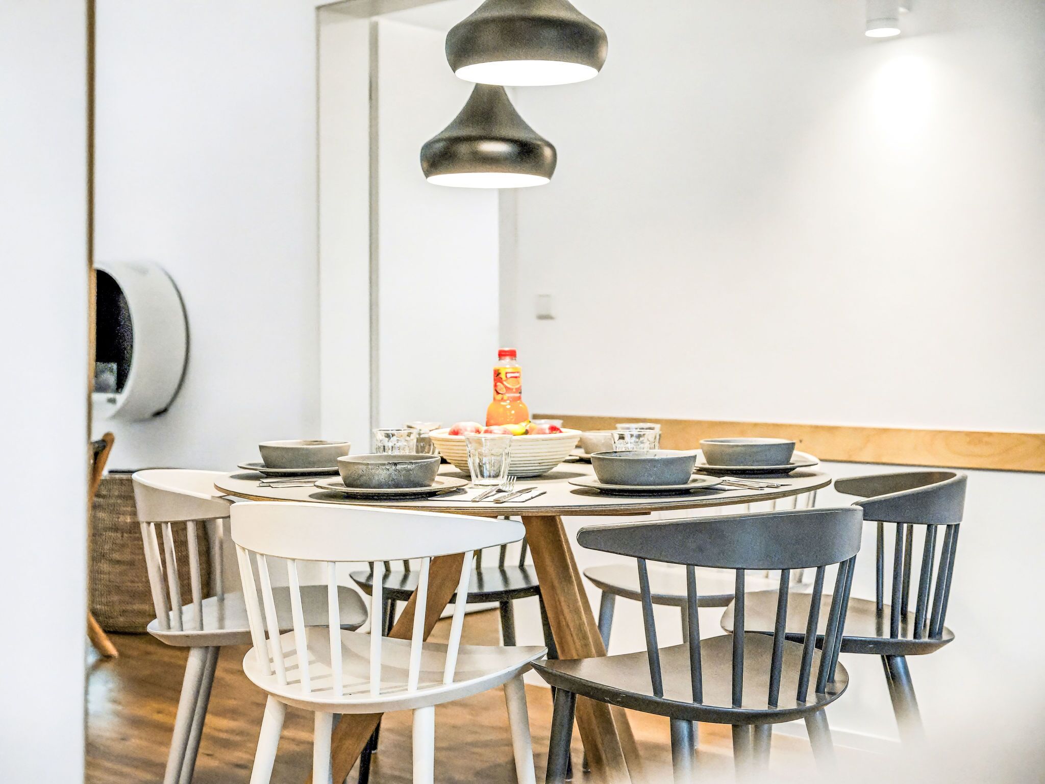 Un coin repas avec une table ronde, six chaises et une bouteille de jus d’orange.