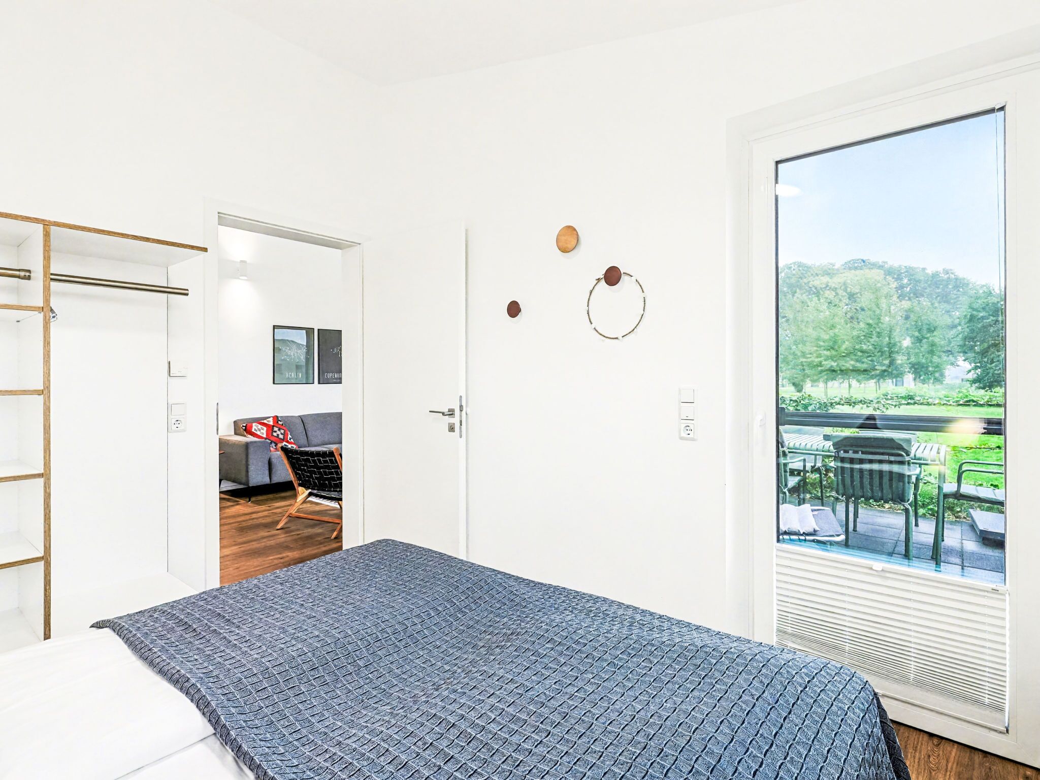 Een moderne hotelkamer met een groot bed, uitzicht op een tuin via een schuifdeur en een zithoek met een bank en stoelen.