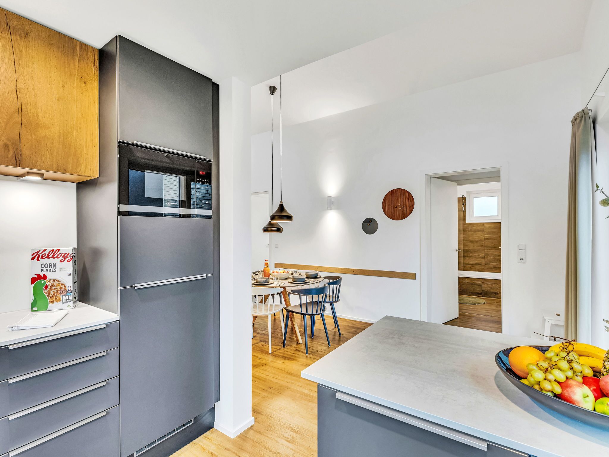 A modern kitchen with grey cabinets, a stainless steel refrigerator, a wooden countertop, and a dining area with a table and chairs.