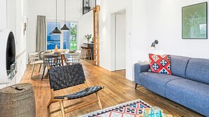 En moderne stue med en blå sofa, et spiseområde med et bord og stole, samt en trappe op til et højere niveau.