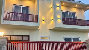 Een tweelaags huis met een rood hekwerk, balkons en buitenverlichting.