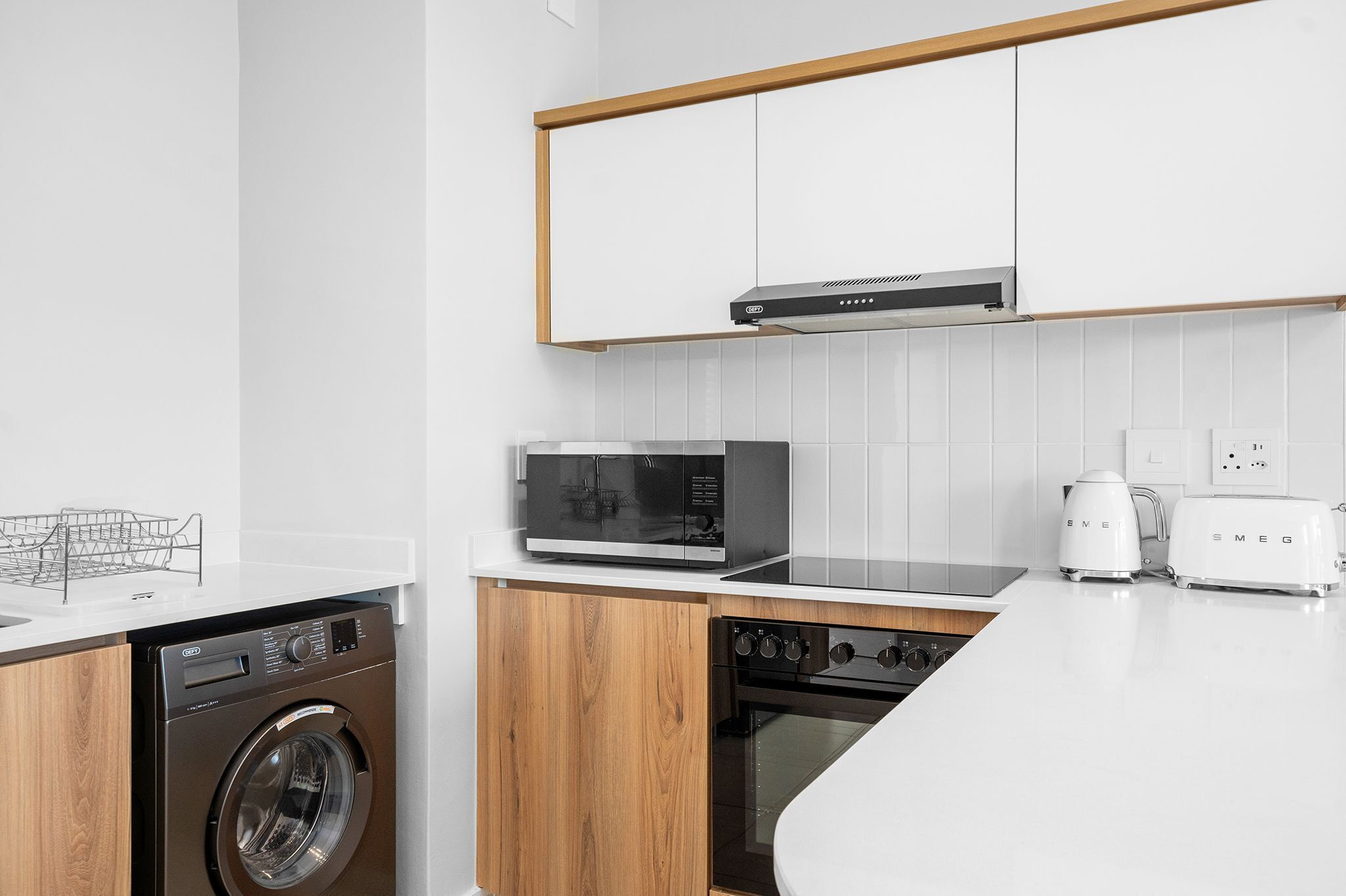 A modern kitchen with a washing machine, microwave, toaster, and oven.