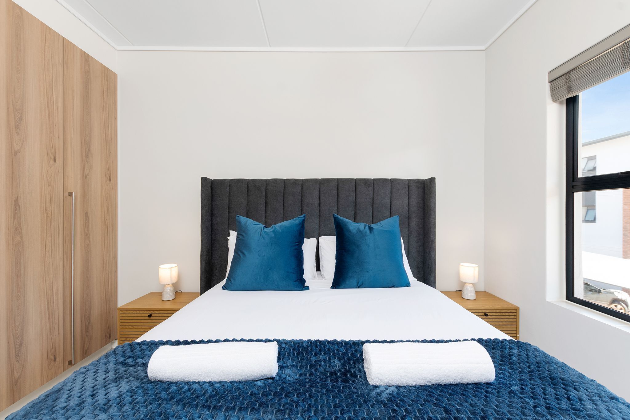 Un dormitorio con cama, dos mesitas de noche, una ventana y un armario.