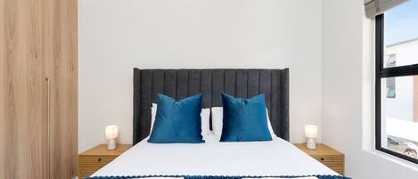 Un dormitorio con cama, dos mesitas de noche, una ventana y un armario.