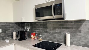 A modern kitchen with white cabinets, a stainless steel microwave, a black induction cooktop, and a tiled backsplash. - Cozy Private Basement Suite (Halifax)