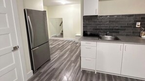 A modern kitchen with white cabinets, a stainless steel refrigerator, and a black tiled backsplash. - Cozy Private Basement Suite (Halifax)