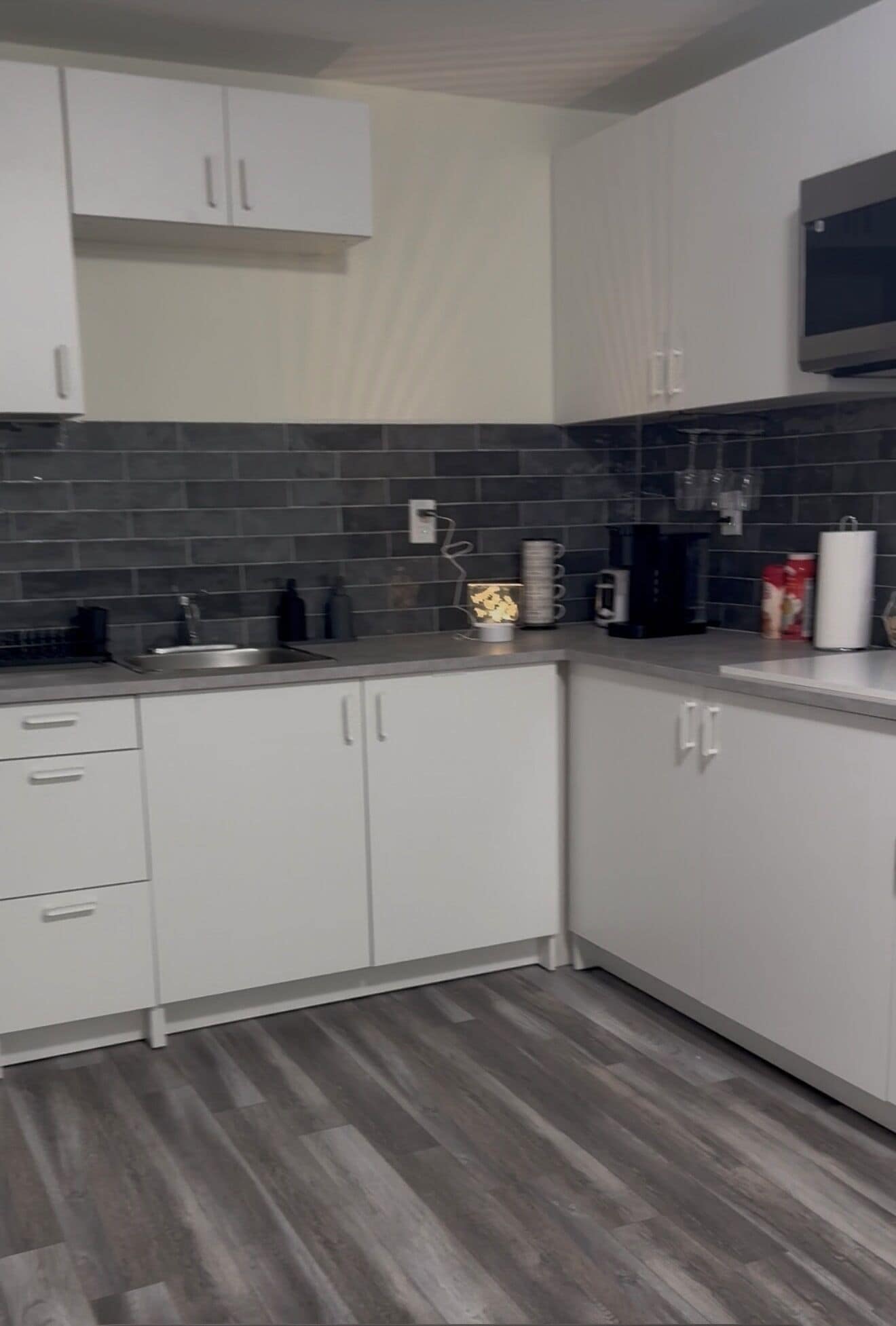 Een moderne keuken met witte kasten, een donkere betegelde spatwand en een grijze houten vloer.