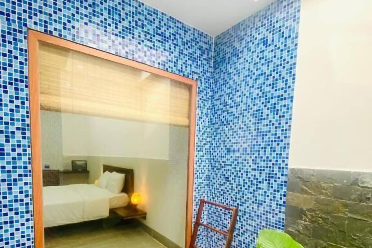 A room with a large mirror, a bed, a nightstand, and a potted plant.