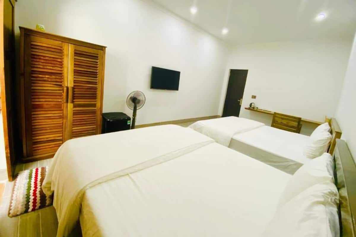 A hotel room with two beds, a wooden wardrobe, a TV, and a desk with a chair.