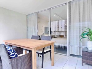 A dining area with a wooden table and wicker chairs, a sliding glass door leading to a balcony, and a potted plant on a table. - @ Marbella Lane- Chic Poolview Home + Patio Dining (Honolulu)
