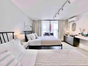 A modern hotel room with a large bed, a desk, a dresser, and a sliding glass door to the balcony. - @ Marbella Lane- Chic Poolview Home + Patio Dining (Honolulu)