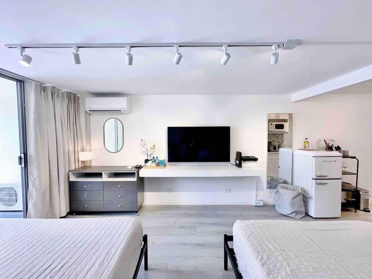 Ein modernes Hotelzimmer mit einem großen Bett, einem kleineren Bett, einem Fernseher, einer Minibar und einem Kühlschrank.