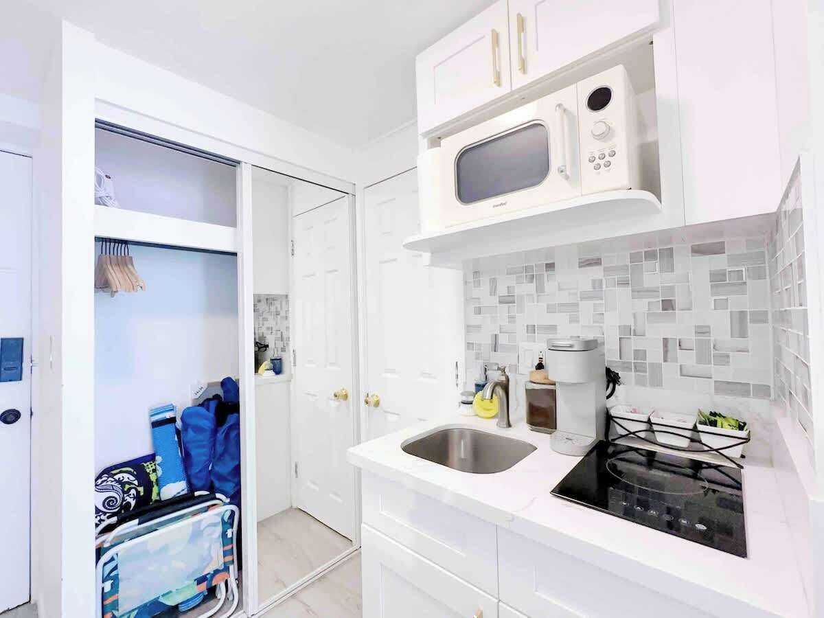 A compact kitchen with white cabinets, a microwave, a sink, and a stove.