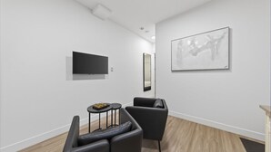 Ein moderner, minimalistischer Raum mit Fernseher, einem großen abstrakten Gemälde und zwei Ledersesseln.