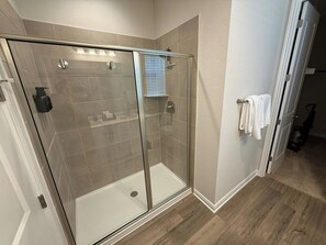 A glass-enclosed shower with a white door, a towel rack, and a light switch on the wall. - The Hofstaat Haus: Modern NB Retreat (New Braunfels)