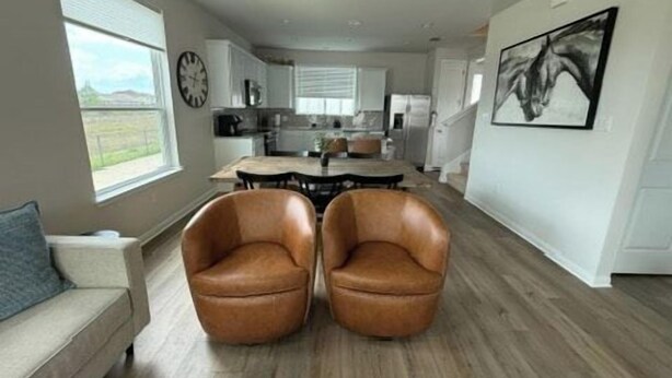 Een moderne keuken met een centraal eiland, een eethoek met twee lederen stoelen, en een woonkamer met een bank.