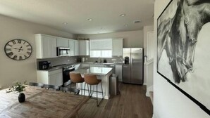 Een moderne keuken met witte kasten, een centraal eiland en een eethoek met een houten tafel en stoelen.