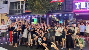 Un gruppo di persone che posa di fronte a un bar e lounge con insegne al neon e il logo Budweiser.