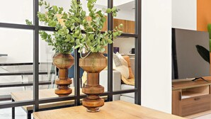 Un soggiorno moderno con un tavolino in legno, due vasi decorativi con piante verdi, un televisore e un divano con cuscini.