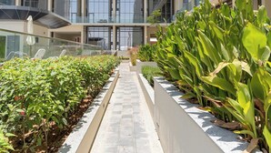 Un edificio moderno con diversi piani, ampie finestre e un percorso centrale affiancato da fioriere con vegetazione.