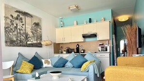 A living room with a sofa, coffee table, and a yellow armchair. There is a kitchen area with cabinets and a microwave. - 2 p+balcony ideally located with splendid view of the Canal Royal and the port of Sète (Sète)