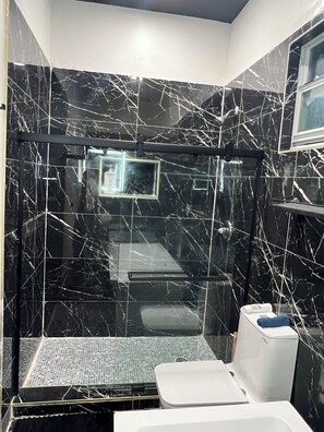 A modern bathroom with black marble walls and a glass shower enclosure. - Stylish 1-Bedroom Private Suite - Miami (Miami)