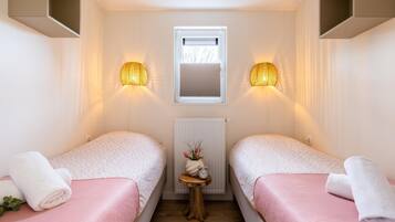 A room with two beds, a small table with a clock, a radiator, and wall-mounted lamps.