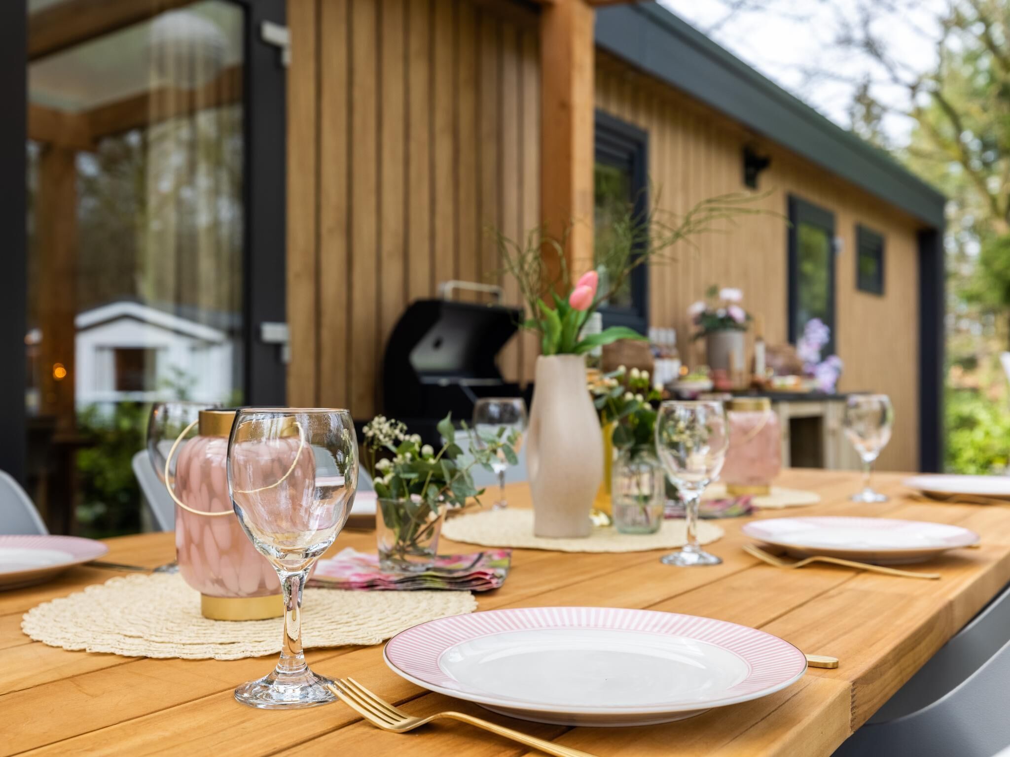 A dining table set with plates, glasses, and cutlery, with a wooden table and a view of a building in the background.