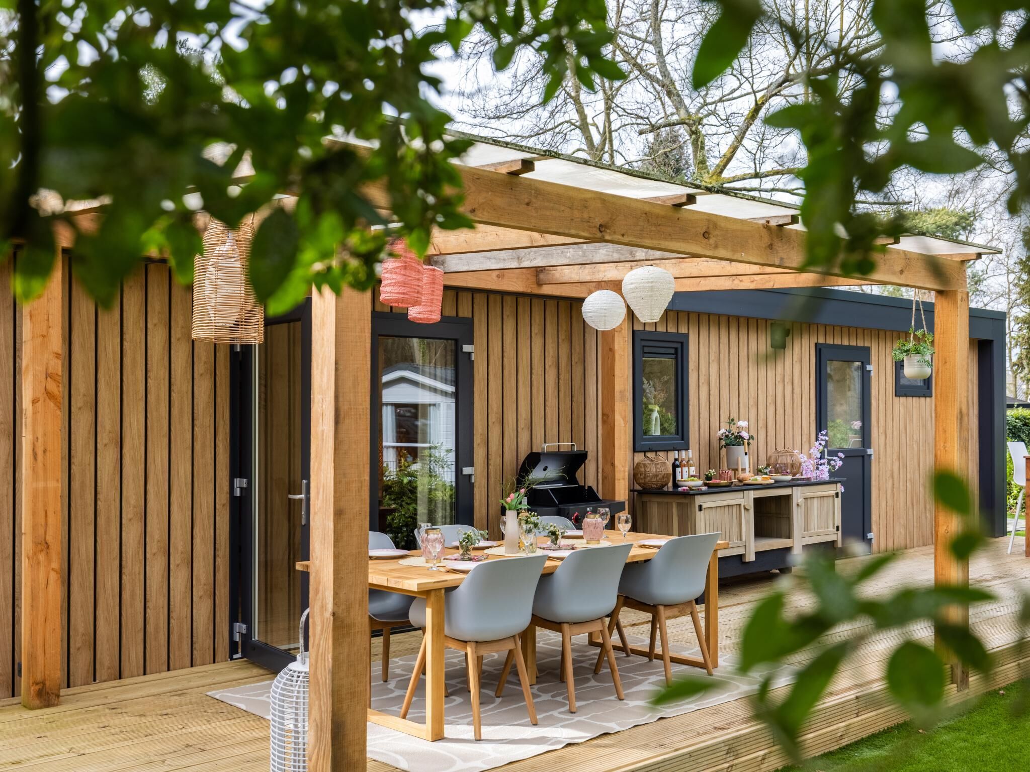 A wooden deck with a dining table and chairs, a grill, and hanging lanterns.