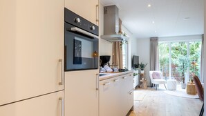 A modern kitchen with white cabinetry, a built-in oven, and a large window overlooking a garden. - Luxury forest stay with covered terrace and BBQ (Hattemerbroek)