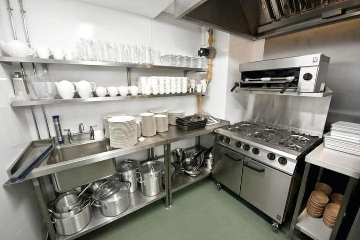 A commercial kitchen with stainless steel appliances, shelves with white dishes, and a sink.