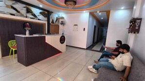 A hotel reception area with a modern design, including a reception desk, a chandelier, and a seating area with two people. - Sky Hotel (Lucknow)