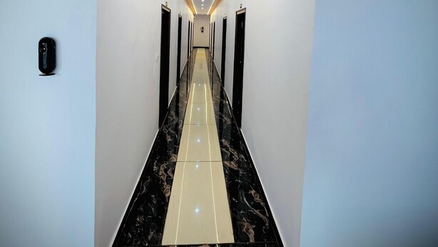 A hallway with a central light strip, black and beige patterned floor, and white walls. - Sky Hotel (Lucknow)