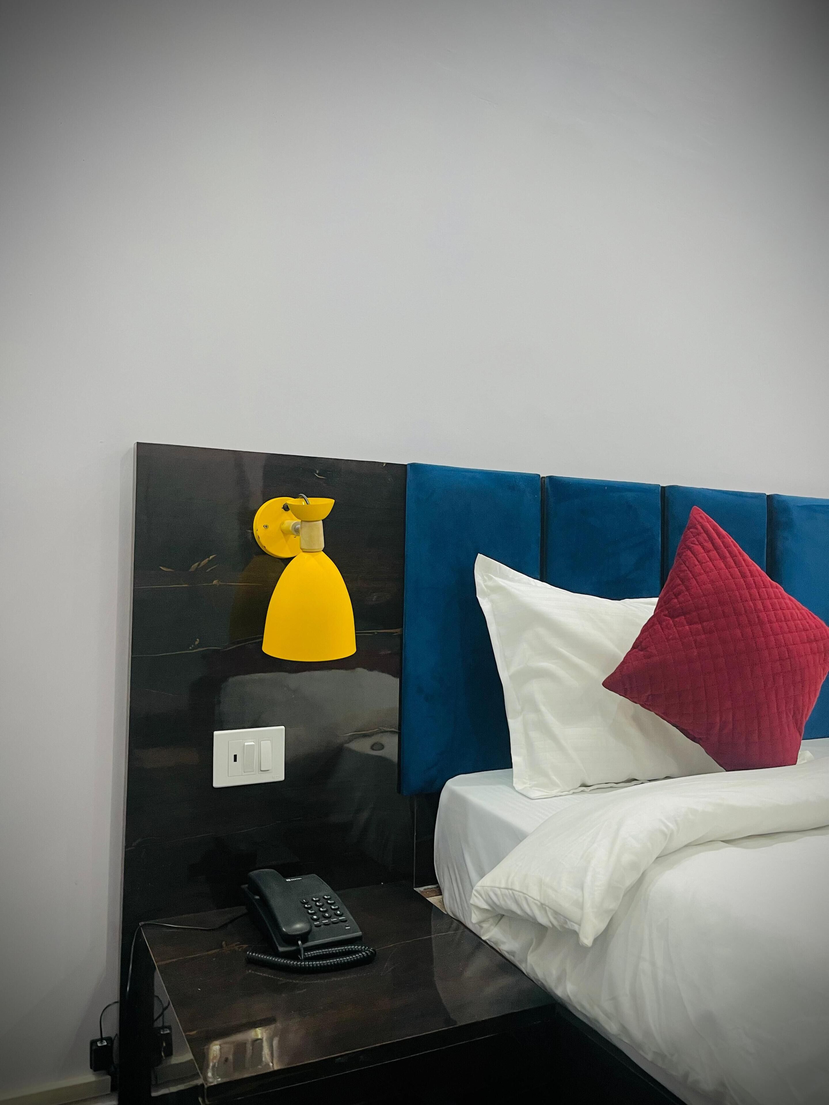 A hotel room with a black headboard, a bedside table with a telephone, and a bed with white and red pillows.