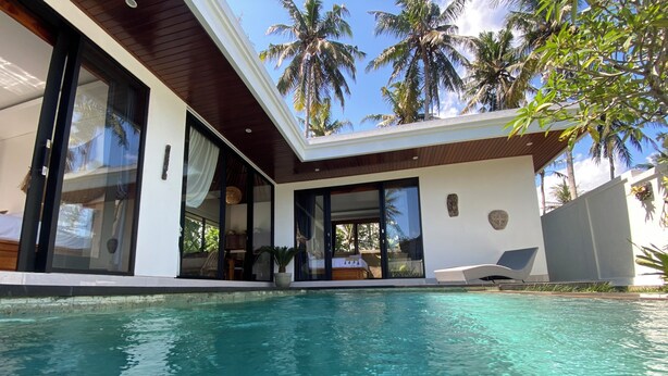 Una casa moderna con piscina, ampie finestre e palme sullo sfondo.
