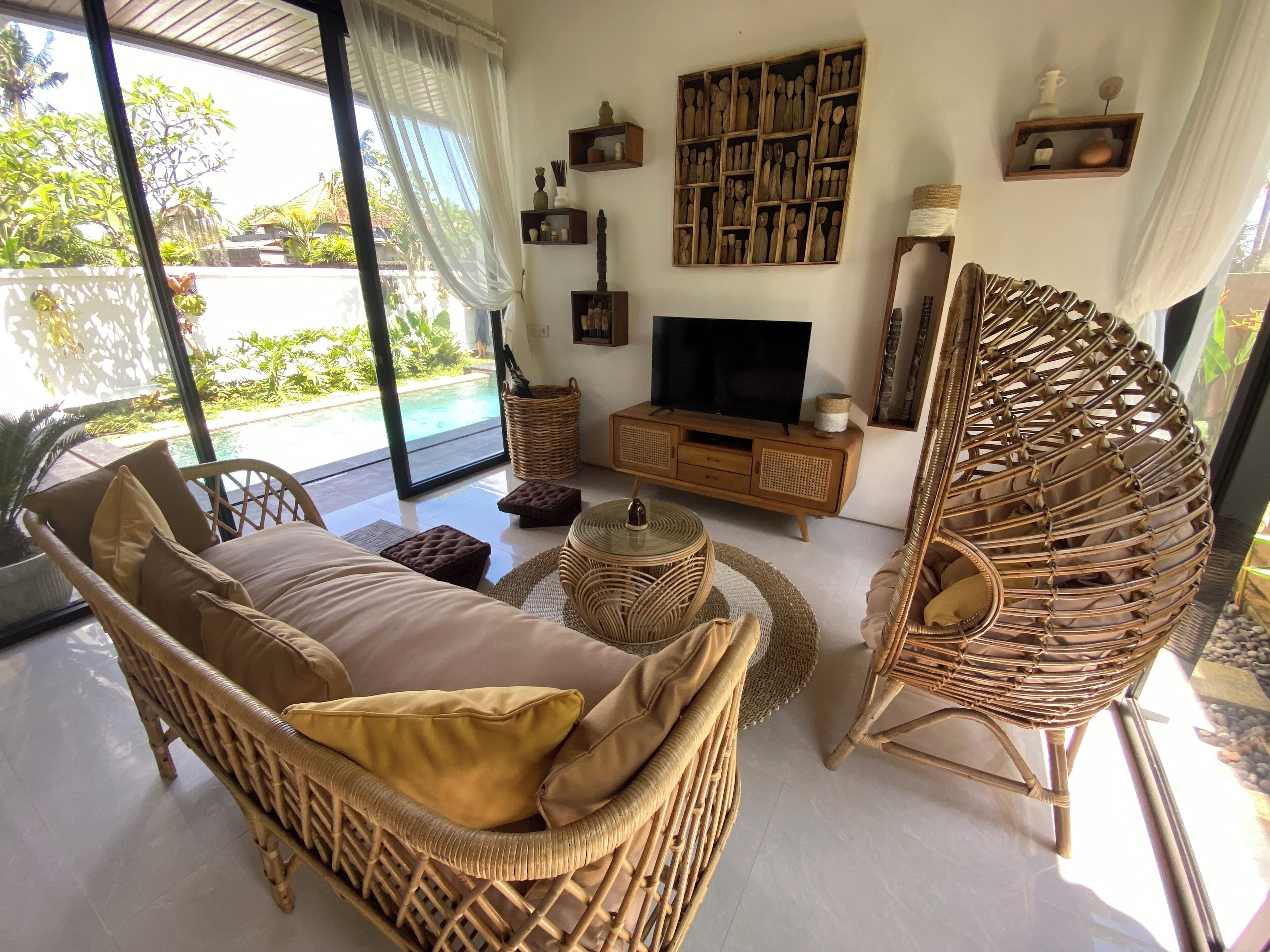 A modern living room with a wicker sofa, a television, and a large window overlooking a pool.
