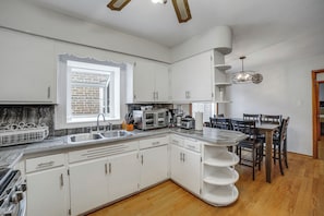 A kitchen with white cabinets, a sink, a stove, and a dining area with a table and chairs.